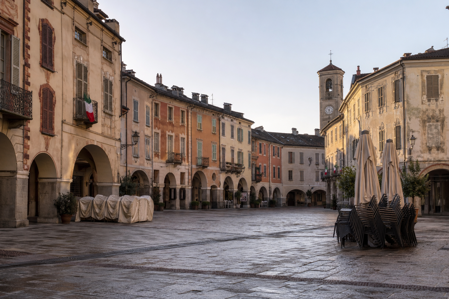 A quiet Piedmont town piazza on an Italian public holiday, with closed shop shutters and Italian flags